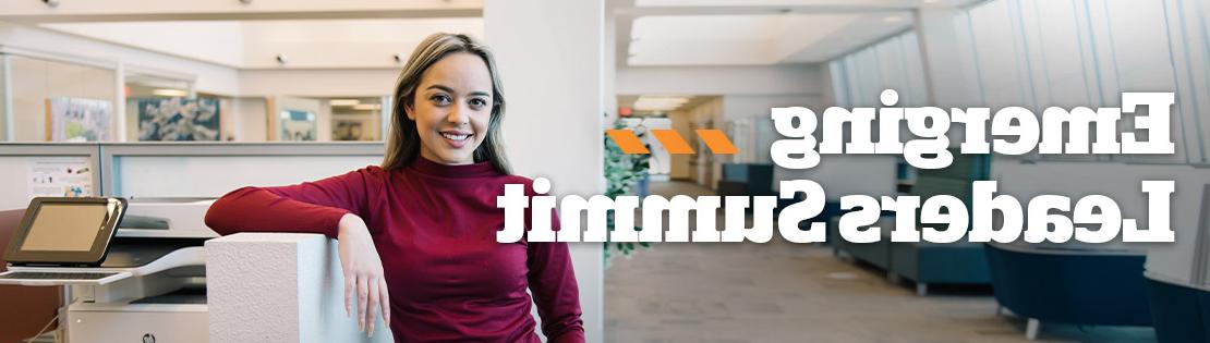 A student smiles at the camera standing in an office space. Associated text says "Emerging Leaders Summit"