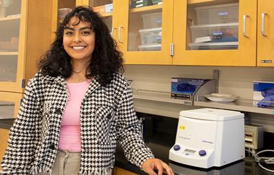 Briana Pomales stans next to a centrifuge in a chem classroom