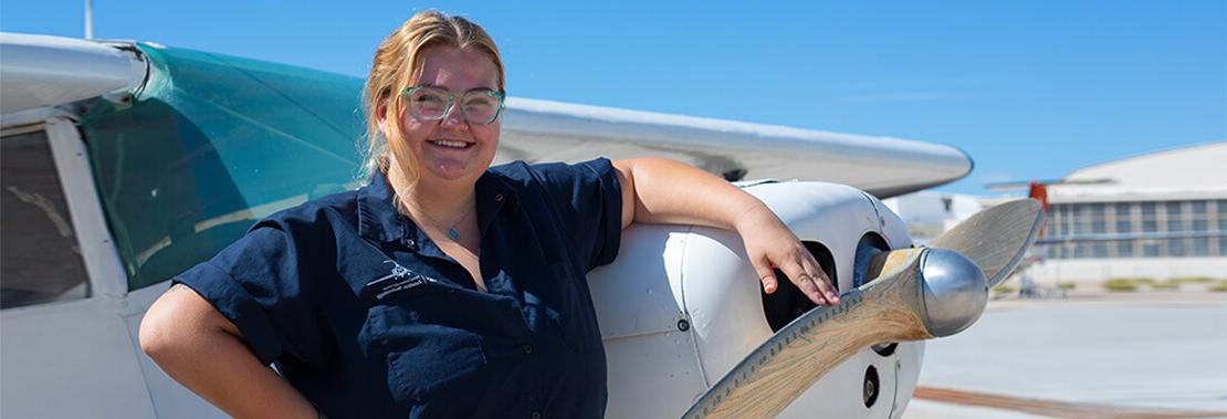 Suzanne Roy stands propped up smiling against a small plane