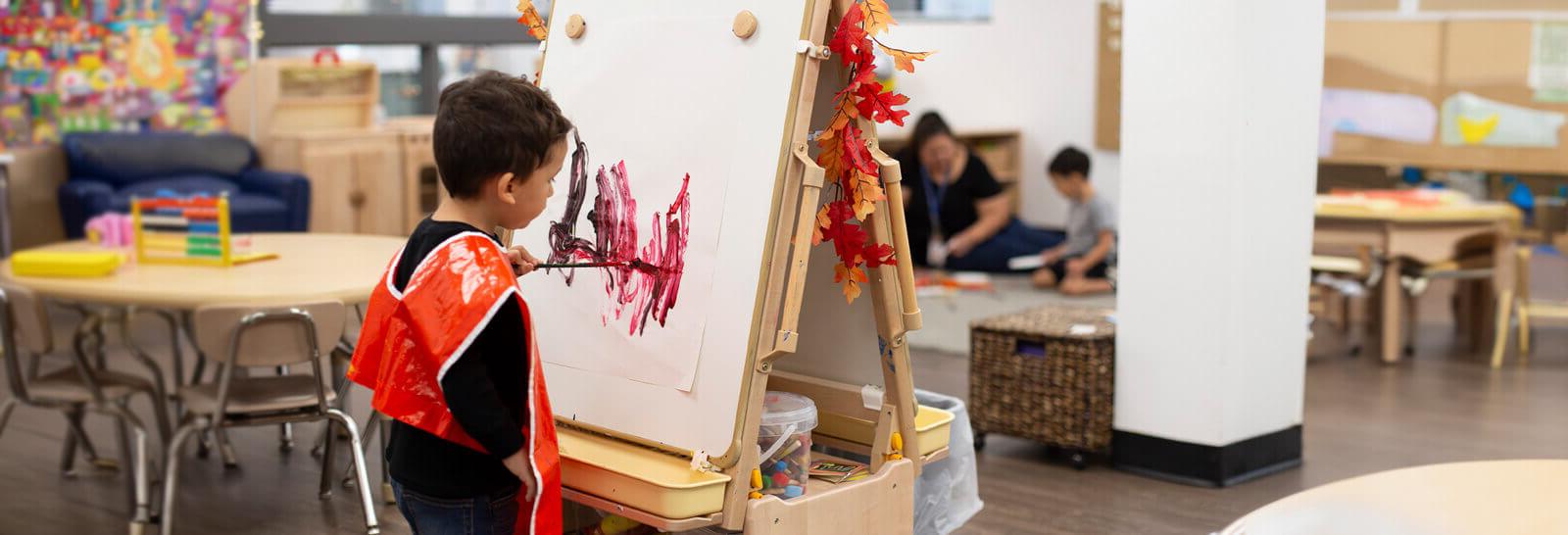 A toddler paints on a canvas in the DV Child Care center