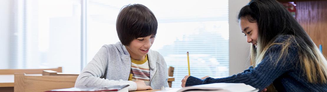 Two pre-teenaged children excitedly work together on a writing activity in a classroom