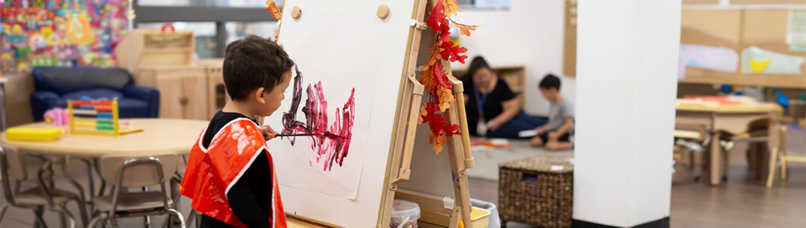 A young Child sits and smiles in a preschool classroom iwth his teachers